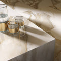 Close-up of Calacatta Oro Complement 60 × 60cm porcelain tiles, highlighting soft white tones with flowing gold veining, styled with reflective glassware to emphasise the polished finish and elegant marble effect.
