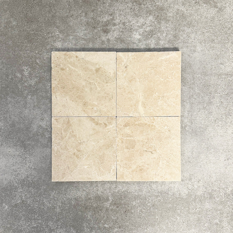 Four Fayrouz Latte Foam 15.2x15.2cm natural marble tiles with a tumbled finish arranged together, showcasing soft cream tones, gentle veining and natural variation against a neutral textured background.