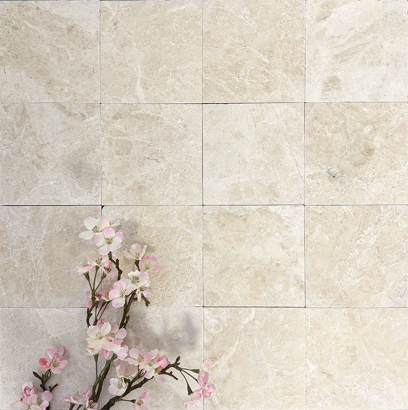 Flat lay of Fayrouz Latte Foam 15.2x15.2cm natural marble tiles with a tumbled finish, featuring soft cream tones and subtle natural veining, styled with delicate pink blossom branches for a calm, elegant look.