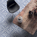 Dining room interior featuring London Streets Thornton Place 20x20cm Victorian Moroccan style porcelain floor tiles in soft blue and white tones, styled with a rustic wooden dining table, black chair and decorative accessories for a classic patterned floor design.