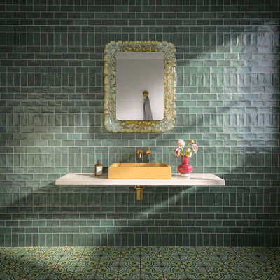 Bathroom featuring Dordogne Green Pines 7.5x15cm rustic gloss wall tiles, showcasing rich green tones with handmade-style shade variation, paired with a white floating vanity, mustard yellow basin, brass fittings, ornate mirror and patterned green floor tiles.