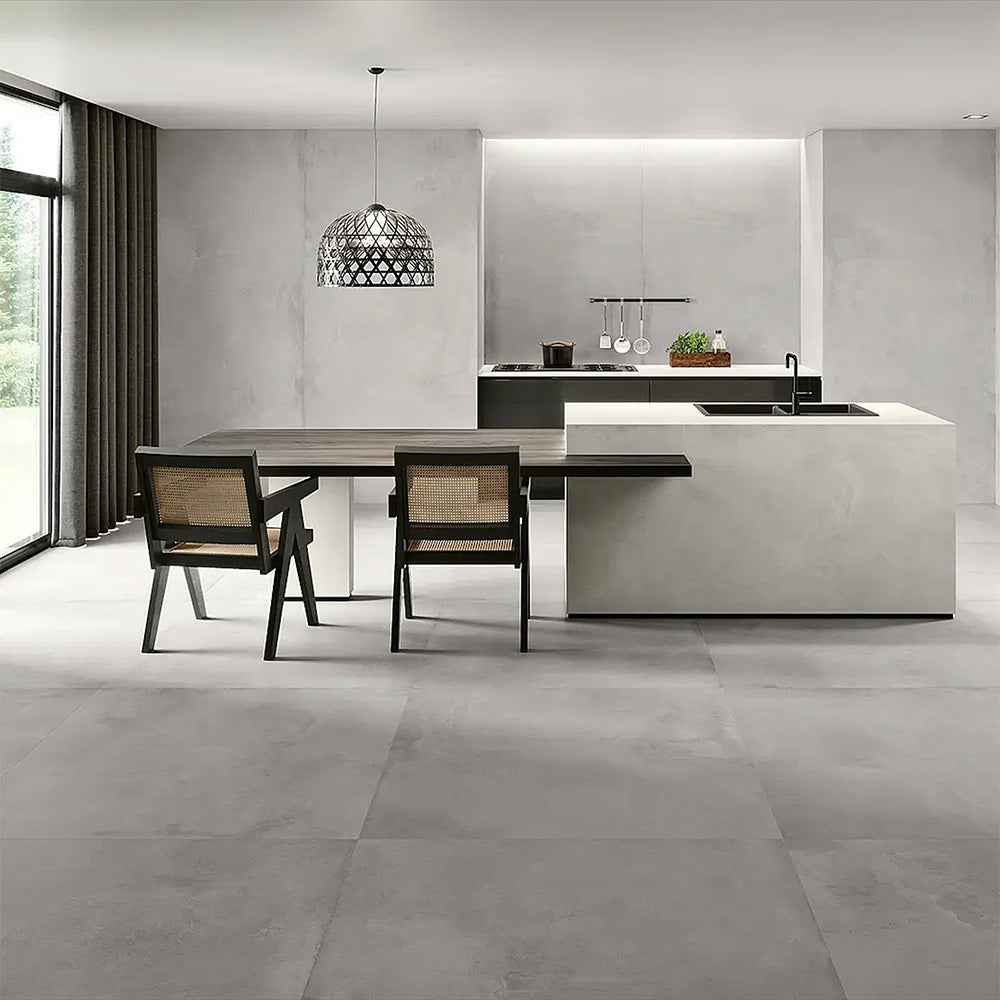 Kitchen interior featuring Etna Grey Matt 30 × 60cm porcelain floor tiles, styled with a modern island, dark cabinetry, woven dining chairs, and soft grey tones for a sleek, contemporary finish.