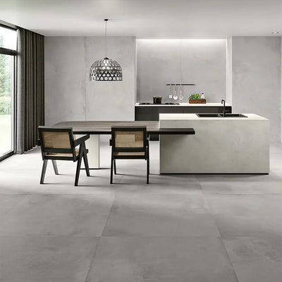 Kitchen interior featuring Etna Grey Matt 30 × 60cm porcelain floor tiles, styled with a modern island, dark cabinetry, woven dining chairs, and soft grey tones for a sleek, contemporary finish.