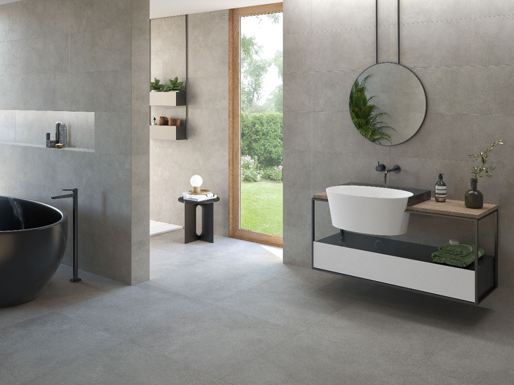 Bathroom interior featuring Etna Grey Matt 60 × 60cm porcelain wall and floor tiles, styled with a freestanding bath, floating vanity, black fittings, and soft grey tones for a calm, contemporary finish.