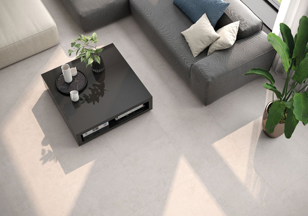 Living room featuring Etna Marfil Matt 30 × 60cm porcelain floor tiles, styled with a grey sofa, black coffee table, indoor plants, and soft natural light for a clean, contemporary finish.