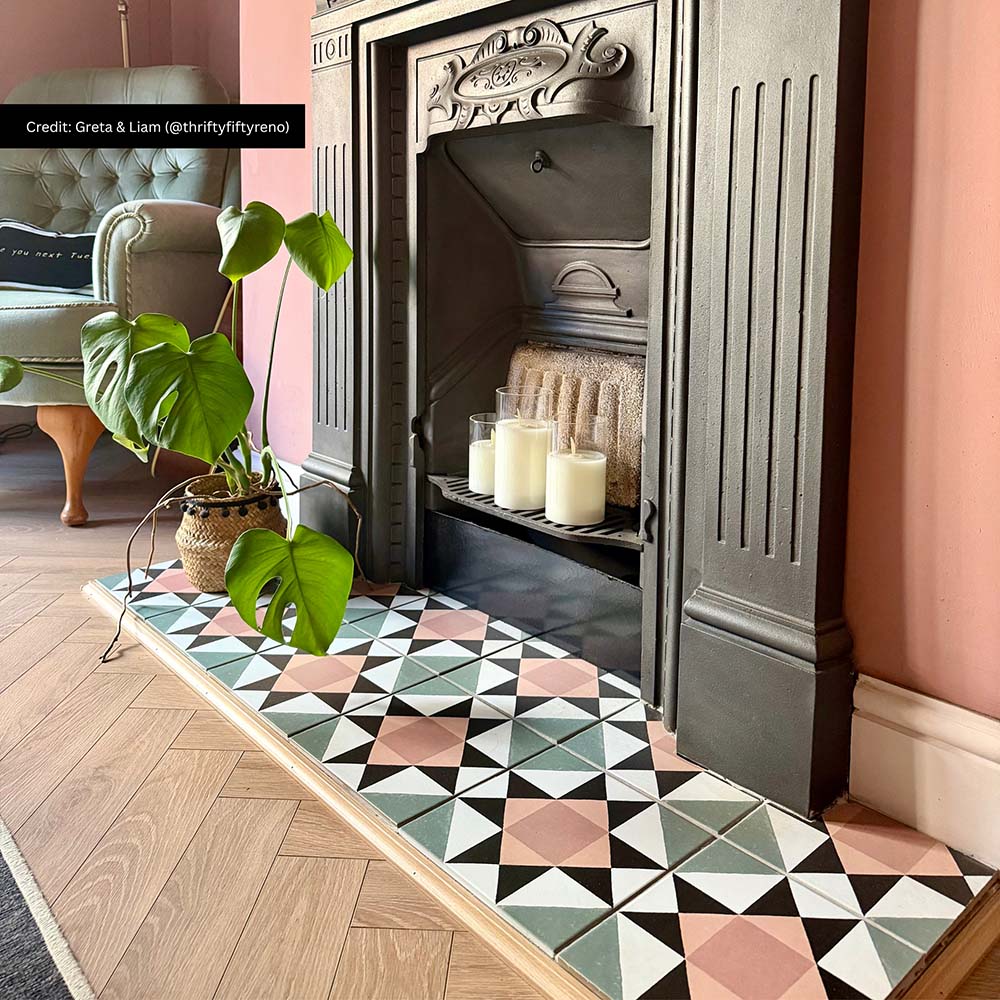 Living room featuring Farnham Manor 20x20cm Victorian-style floor tiles, styled as a decorative fireplace hearth with soft pink walls, herringbone wood flooring, period features and botanical accents.