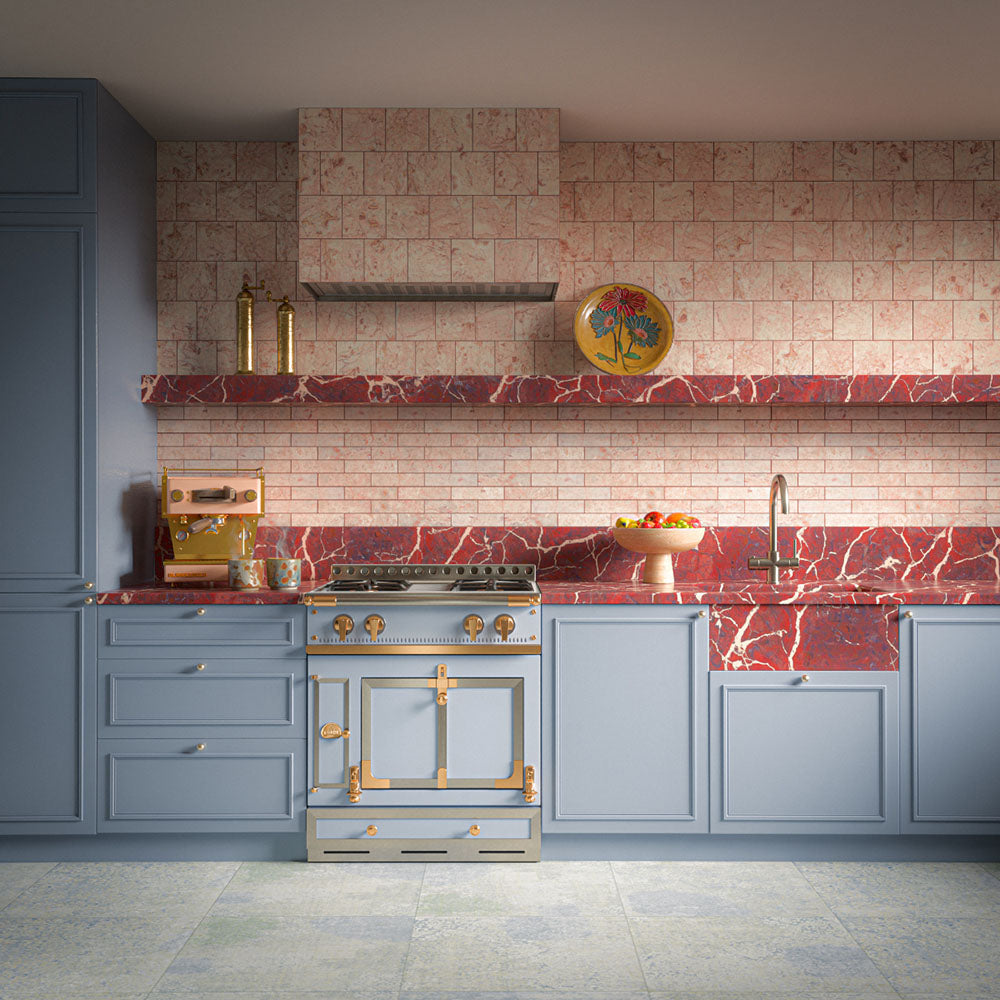 Kitchen featuring Fayrouz Sylvester Pink Honed Finish Natural Marble 5cm x 20cm splashback tiles, laid in a brick pattern and paired with blue shaker cabinetry, red marble worktops, brass fittings and a traditional range cooker.
