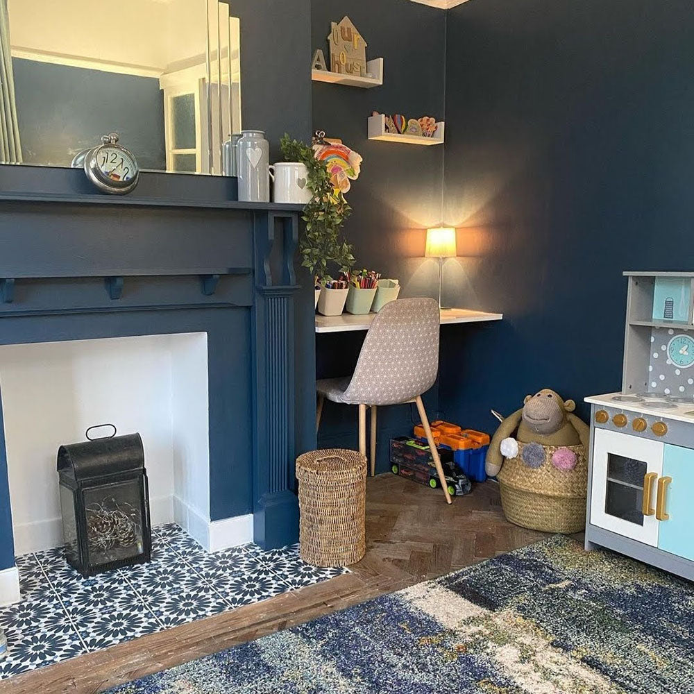 Living room fireplace hearth featuring Fez Federal Blue 20x20cm Moroccan-style porcelain tiles, showcasing a bold blue and white geometric pattern, paired with deep navy walls, warm wood flooring and a cosy family-friendly interior.