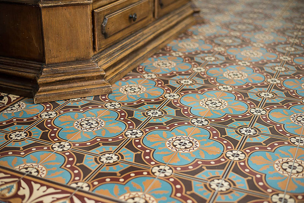 Interior floor setting featuring London Streets Hanover Square 20x20cm Victorian Moroccan style floor tiles, showcasing the repeating blue, terracotta and cream geometric pattern, styled alongside a traditional wooden cabinet for a classic decorative floor design.