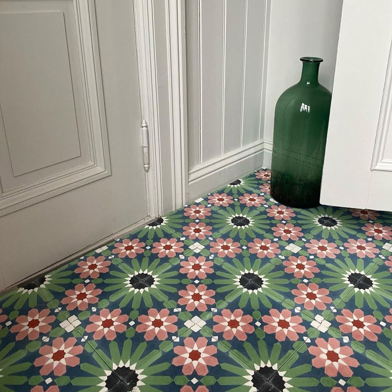 Floor featuring Fez Autumn 20x20cm Moroccan-style porcelain tiles, displaying a bold geometric floral pattern in deep green, terracotta and soft blush tones, styled in a hallway setting with white panelled walls and a decorative green glass bottle.
