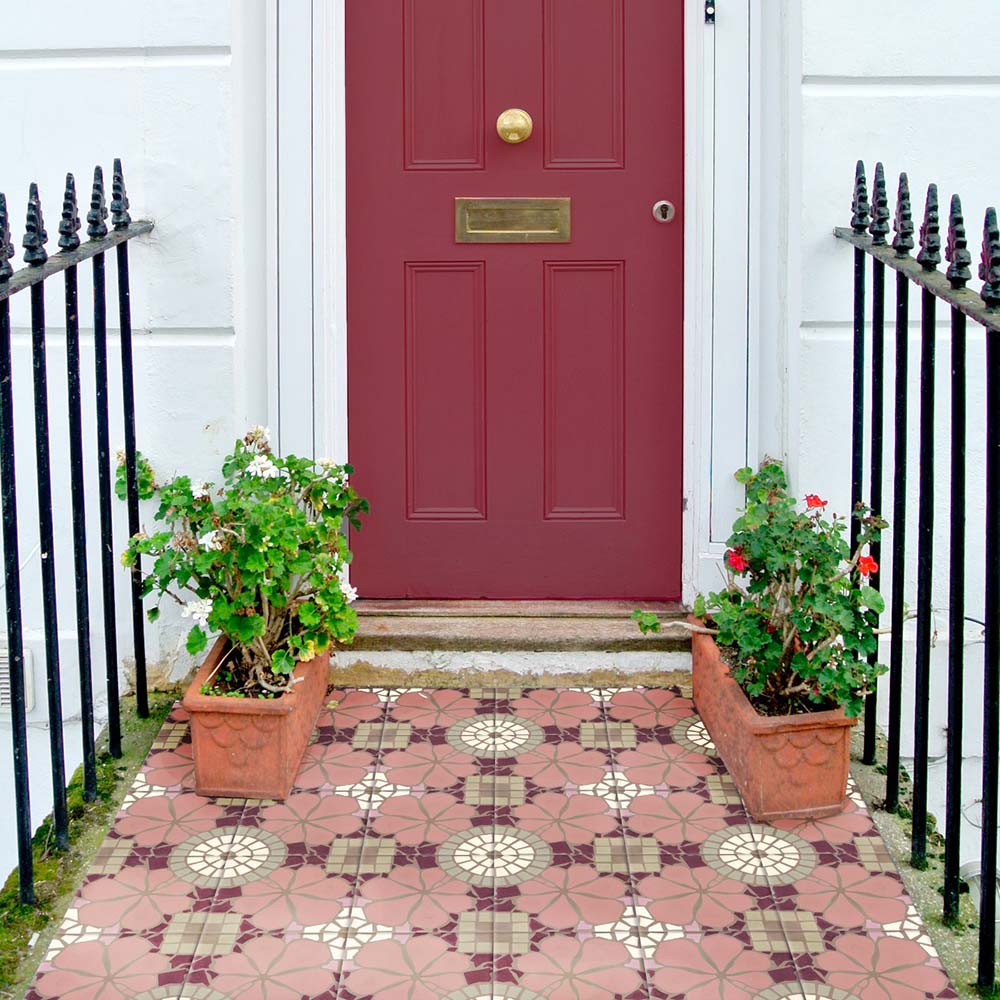Nantes Rose Pink Moroccan-style tiles laid at a front entrance, creating a decorative tiled doorstep. The 20x20cm patterned tiles feature soft pink floral motifs with cream circular detailing and subtle geometric accents, beautifully complementing the deep red front door and classic townhouse exterior.