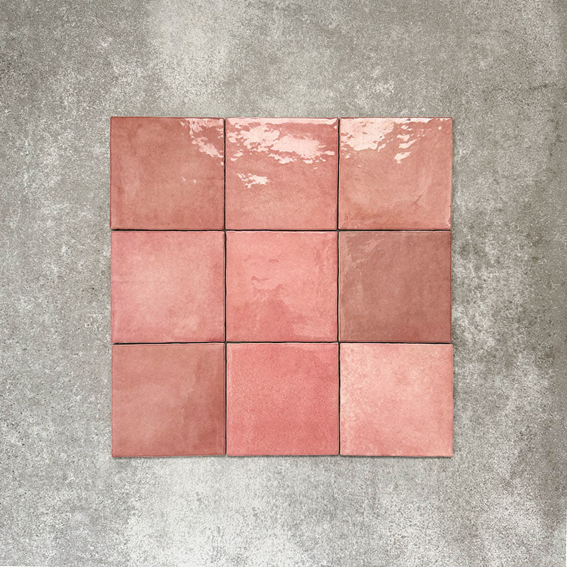 Flat lay of Zellige Rose Pink Square 13.2 × 13.2cm Moroccan-style ceramic tiles in soft blush, dusty rose and warm pink tones, showing subtle shade variation and gently uneven edges, arranged in a simple grid on a textured grey background to highlight the handcrafted zellige-effect surface.