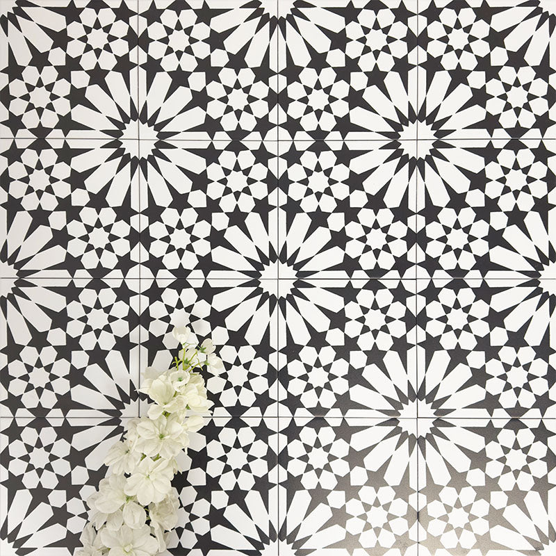 Fez Winter Moroccan-style porcelain tiles laid in a repeating pattern, showcasing a striking black and white geometric star design. The 20 × 20cm tiles create a bold, high-contrast encaustic-effect surface, styled with white florals to highlight the crisp detailing and symmetry. Ideal for statement floors, feature walls, splashbacks, and contemporary or monochrome interior schemes.