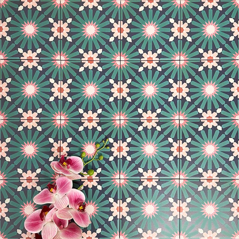 Fez Mini Festival 15x15cm Moroccan-style porcelain wall tiles arranged in a repeating geometric pattern, featuring bold teal, pink and warm neutral star motifs, styled with pink orchid flowers for a vibrant, decorative finish.