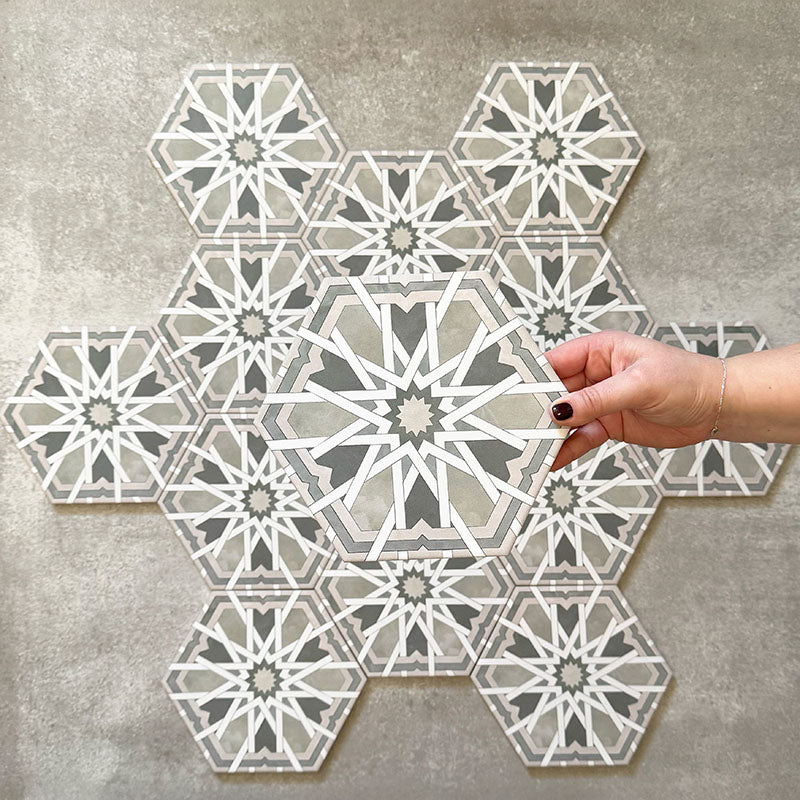 Hand holding Medina Hormuz Sage Green/Grey Moroccan-style hexagon porcelain tile, 18.7 × 21.6 cm, shown against a grouped layout to highlight the bold star-inspired geometric pattern in sage green, grey and white tones.