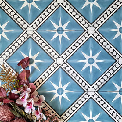 Gilgamesh Blue Moroccan style 20x20cm patterned tiles, shown in a flat lay with decorative foliage highlighting the blue, black and white geometric star design.