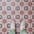 Fez Rosso Moroccan-style porcelain tiles laid in a neat grid, creating a rich, rhythmic pattern across the floor. Warm terracotta red starbursts sit against a soft grey-blue base, balanced by delicate blush pink and white geometric details inspired by traditional Moroccan tilework. Styled here with neutral footwear for scale, the design feels bold yet refined—perfect for adding warmth and character to kitchens, hallways or statement floor spaces while remaining practical and durable in porcelain.