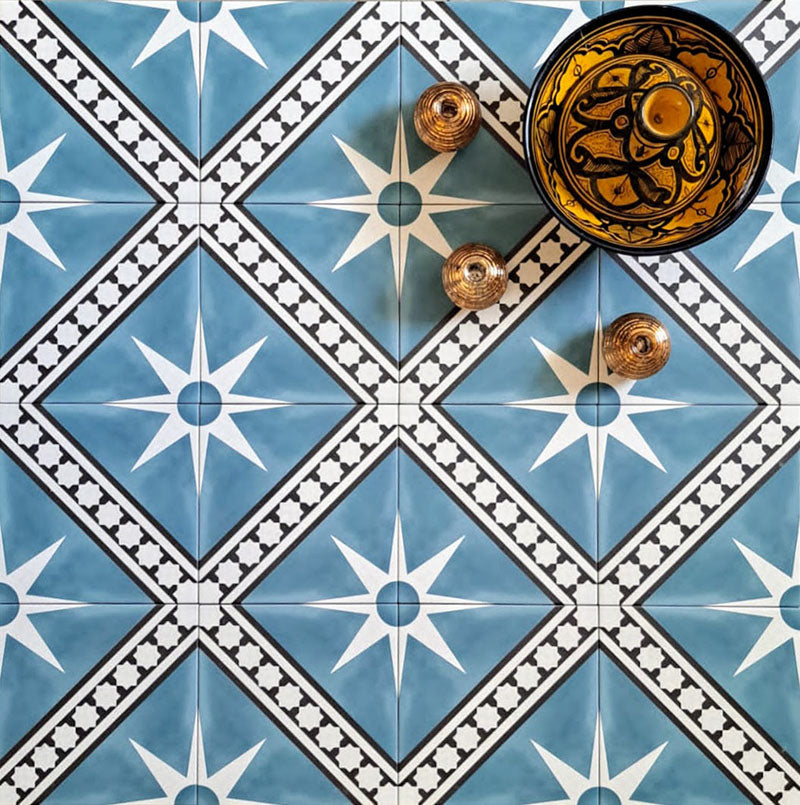 Gilgamesh Blue Moroccan style 20x20cm patterned tiles, shown in a flat lay with decorative foliage highlighting the blue, black and white geometric star design.