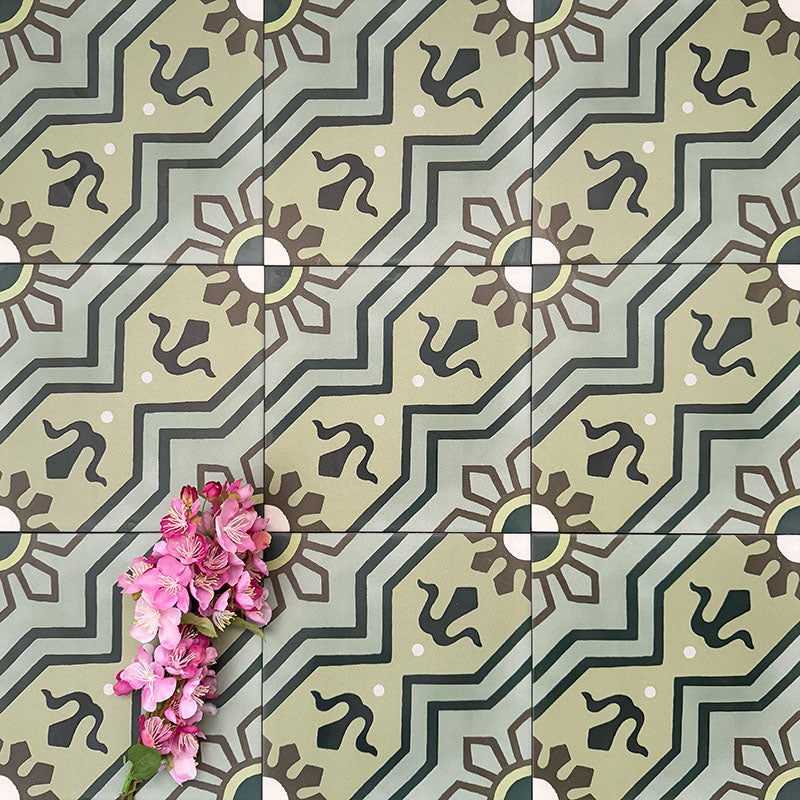 Close-up of Balthazar Verde 20×20cm Moroccan-style porcelain tiles laid in a repeating pattern, highlighting the encaustic-inspired geometric design in layered green tones with dark accents, styled with pink flowers to emphasise the intricate detailing and matt finish.
