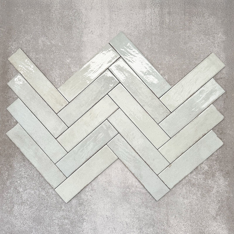 Nomad Mint Green brick wall tiles in a 6 × 24.6cm format, shown laid together in a herringbone to highlight the soft green colour, gloss finish and subtle surface variation.