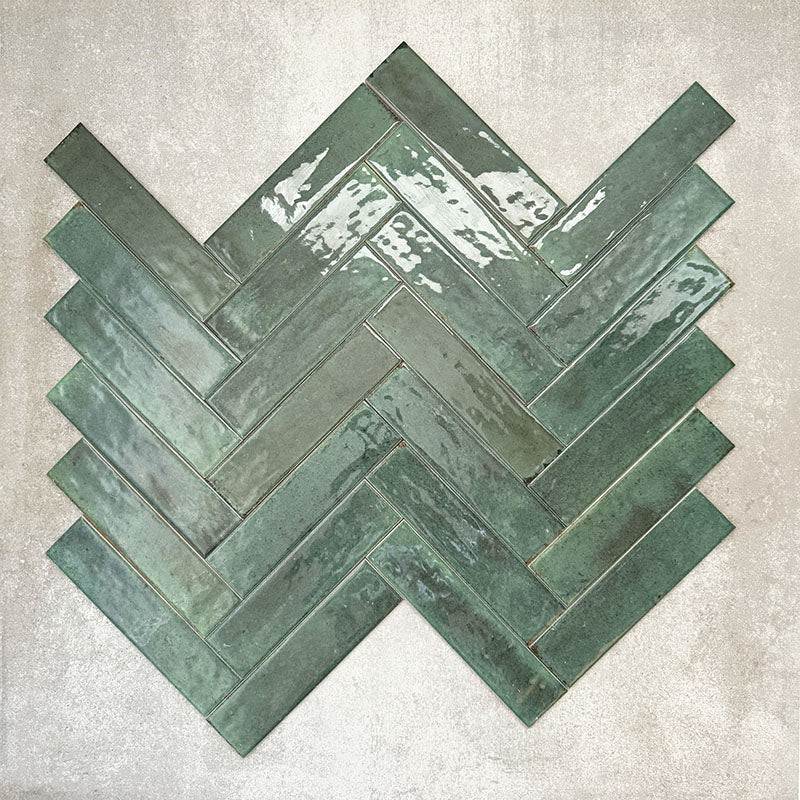 Allegra Green Gloss Brick ceramic tiles in a 6 × 25cm format, arranged in a herringbone pattern to showcase the deep green colour, high-gloss finish and subtle handmade-style surface variation.