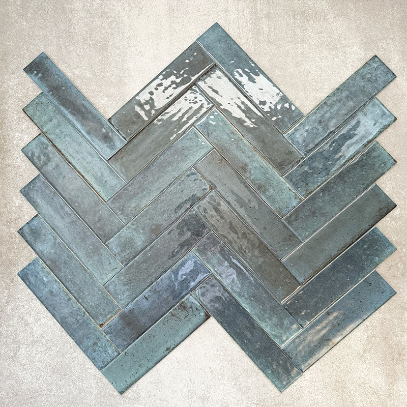 Allegra Blue Gloss Brick ceramic tiles in a 6 × 25cm format, arranged in a herringbone pattern to showcase the rich blue tones, glossy finish and subtle handmade-style variation.