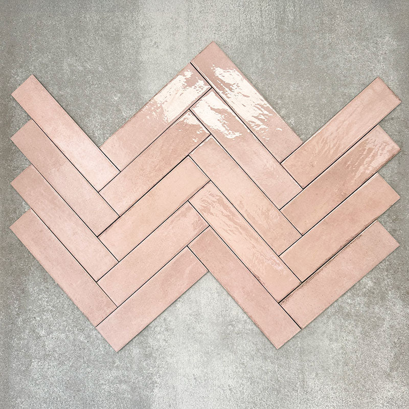 Nomad Rose brick wall tiles in a 6 × 24.6cm format, shown laid together in a herringbone layout to highlight the soft pink tone, gloss finish and subtle surface variation.