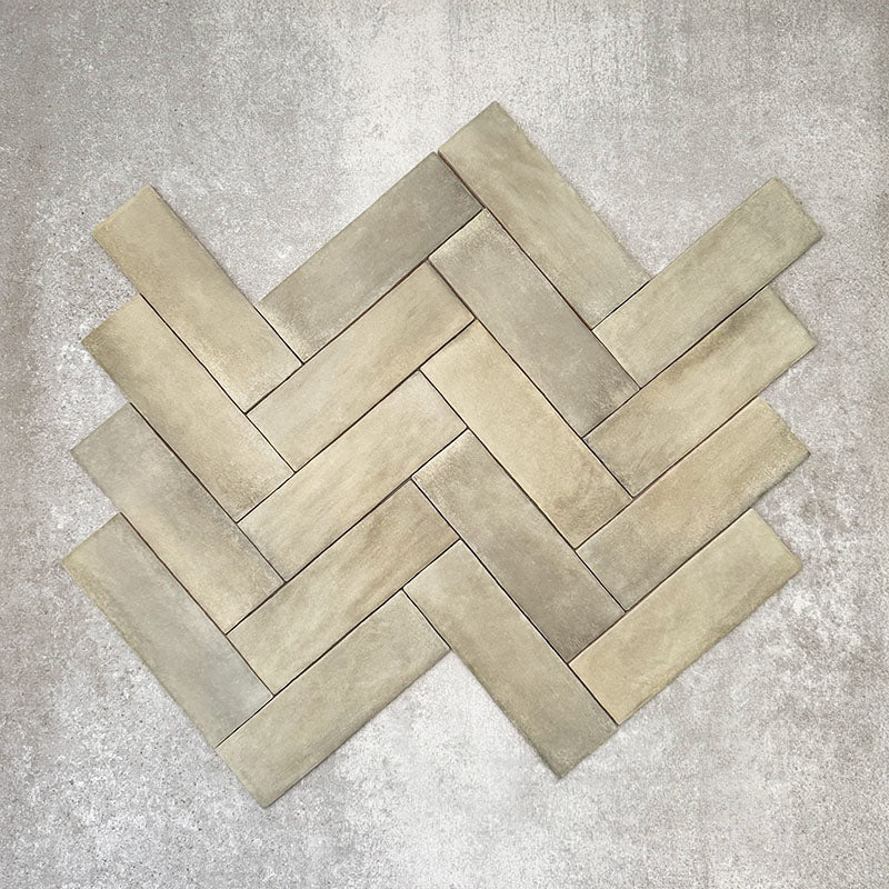 Flat lay of Zellige Weald Green 6.5×20cm Moroccan-style ceramic brick tiles, shown in a herringbone layout, highlighting soft green and earthy tonal variation, irregular edges and a handmade-look glazed finish on a neutral background.