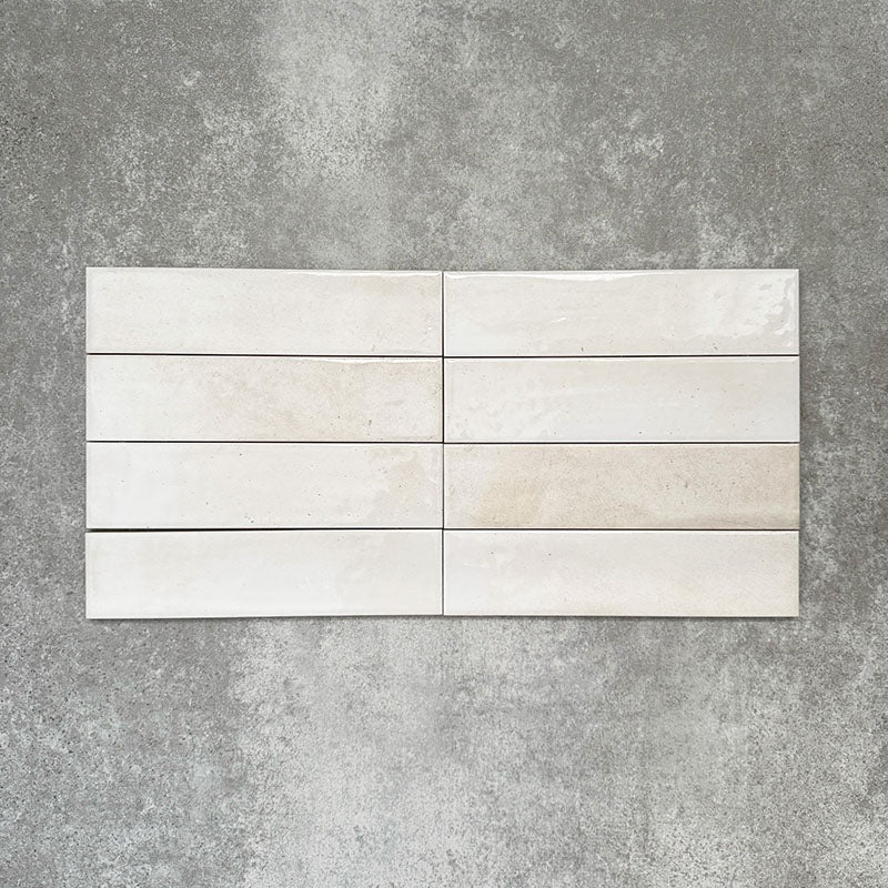 Allegra Blanca Gloss Brick ceramic tiles in a 6 × 25cm format, laid horizontally to emphasise the glossy white finish and gentle tonal variation of the handmade-style surface.