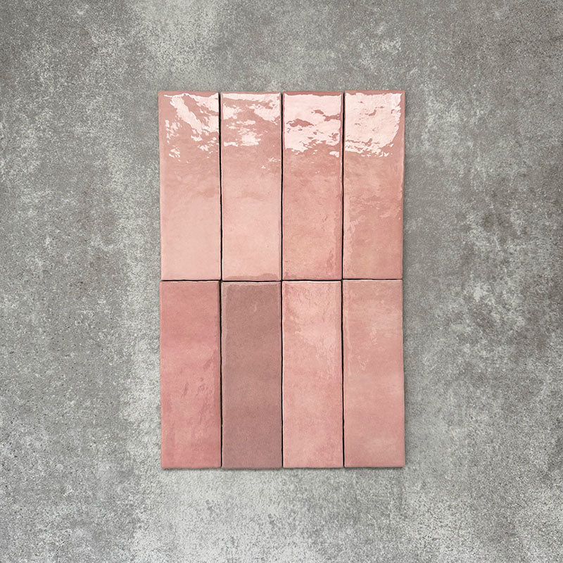 Flat lay of Zellige Rose Pink Brick 6.5 × 20cm Moroccan-style ceramic tiles, shown in soft blush, dusty rose and terracotta pink tones with gentle tonal variation and lightly uneven edges, arranged in a vertical brick layout on a textured grey background to showcase the handcrafted zellige-effect glaze.