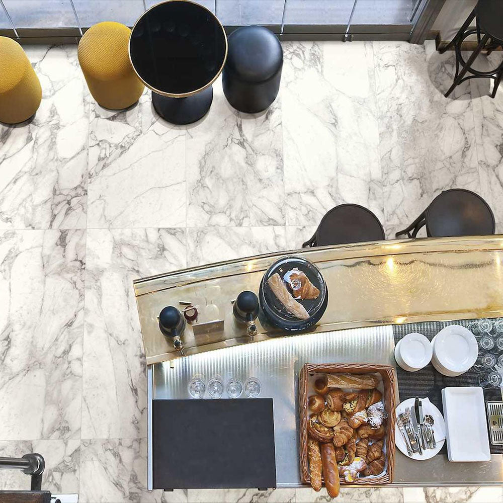 Top-down view of Hudson Calacatta Matt Marble 30 × 60cm porcelain floor tiles, showcasing a soft white base with elegant grey veining, styled within a café setting with warm metallic accents and contemporary furnishings for a refined, modern look.
