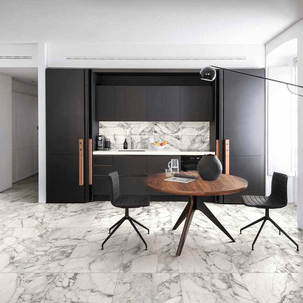 Modern kitchen and dining space featuring Hudson Calacatta Matt Marble 60 × 60cm porcelain floor tiles, showcasing a crisp white base with soft grey veining, paired with dark cabinetry, warm wood tones, and minimalist styling for a clean, contemporary finish.