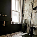 Bathroom interior featuring Hudson Capraia Matt Marble 60 × 60cm porcelain wall and floor tiles, styled with bold dark veining against a soft white base, paired with black fixtures and warm brass accents for a striking, contemporary contrast.