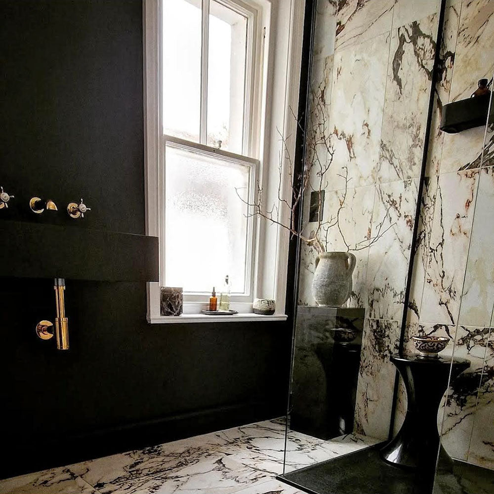 Bathroom interior featuring Hudson Capraia Matt Marble 60 × 60cm porcelain wall and floor tiles, styled with bold dark veining against a soft white base, paired with black fixtures and warm brass accents for a striking, contemporary contrast.