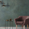 Living space detail featuring Iron Emerald Green Oxide Metallic 60 × 60cm porcelain wall tiles, showcasing deep green tones with subtle tonal variation and a soft metallic effect, paired with warm upholstery, light wood legs, and minimal styling for a calm, contemporary contrast.