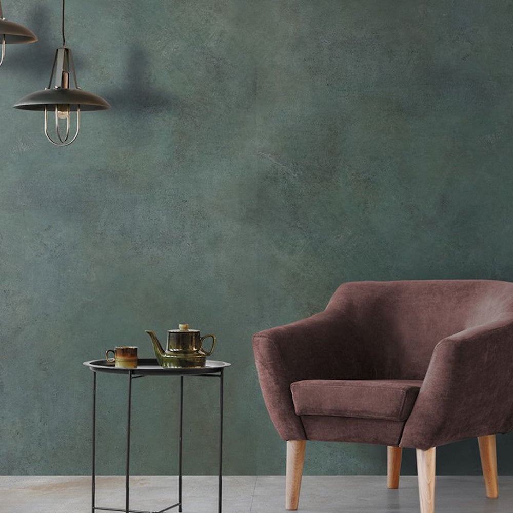 Living space detail featuring Iron Emerald Green Oxide Metallic 60 × 60cm porcelain wall tiles, showcasing deep green tones with subtle tonal variation and a soft metallic effect, paired with warm upholstery, light wood legs, and minimal styling for a calm, contemporary contrast.