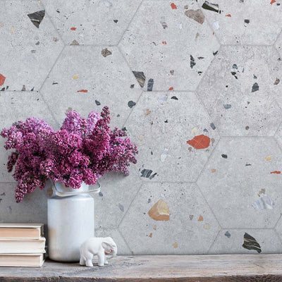 Styled interior wall featuring Jericho Silver Terrazzo Hexagon 25 × 22cm porcelain tiles, with a soft grey base and scattered multicoloured aggregate chips, laid in a honeycomb pattern and paired with natural wood and floral accents for a calm, contemporary feel.