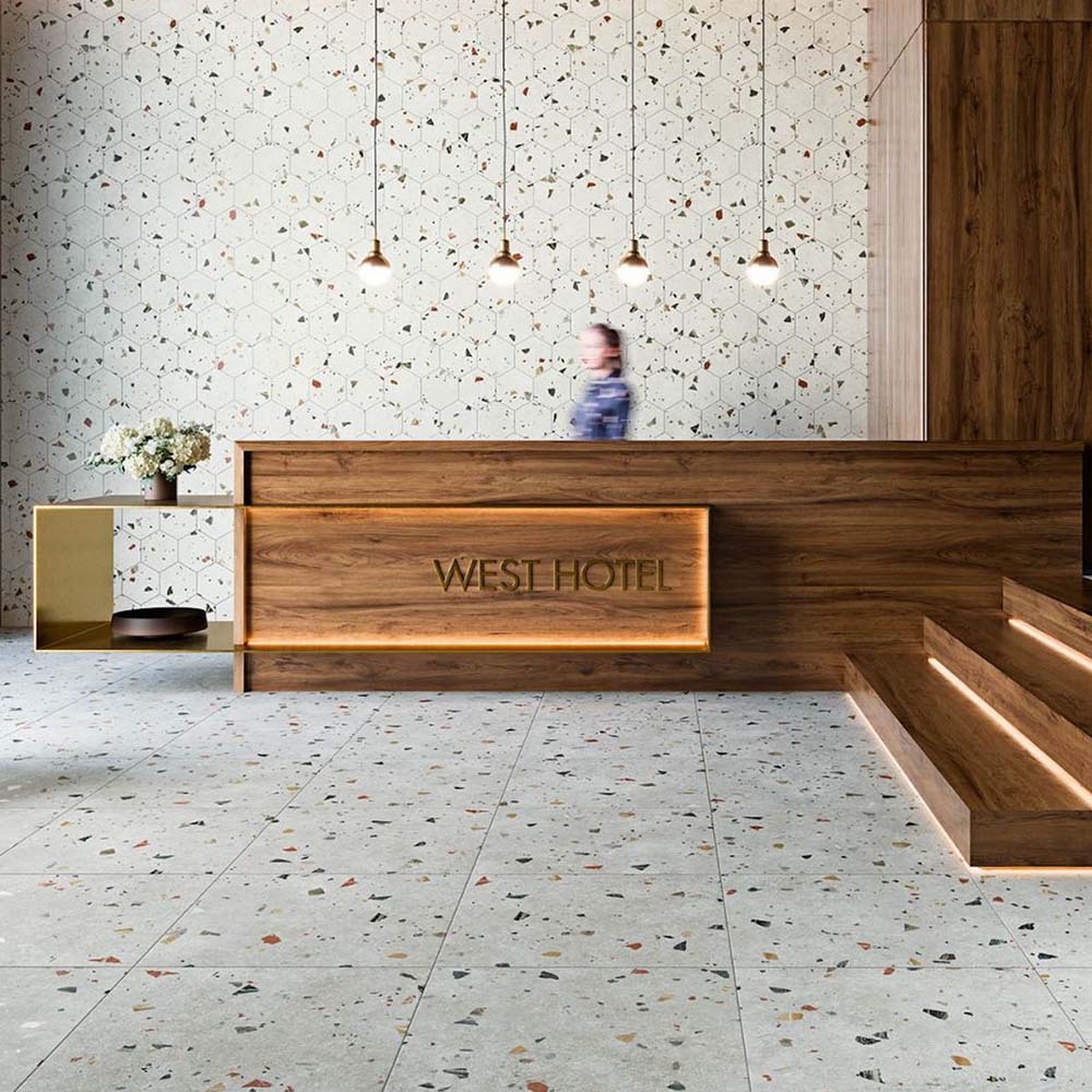 Hotel reception interior featuring Jericho Silver Terrazzo 66 × 66cm porcelain wall and floor tiles, with a soft grey base and scattered multicoloured aggregate chips, paired with warm wood panelling and minimalist lighting for a refined, contemporary setting.