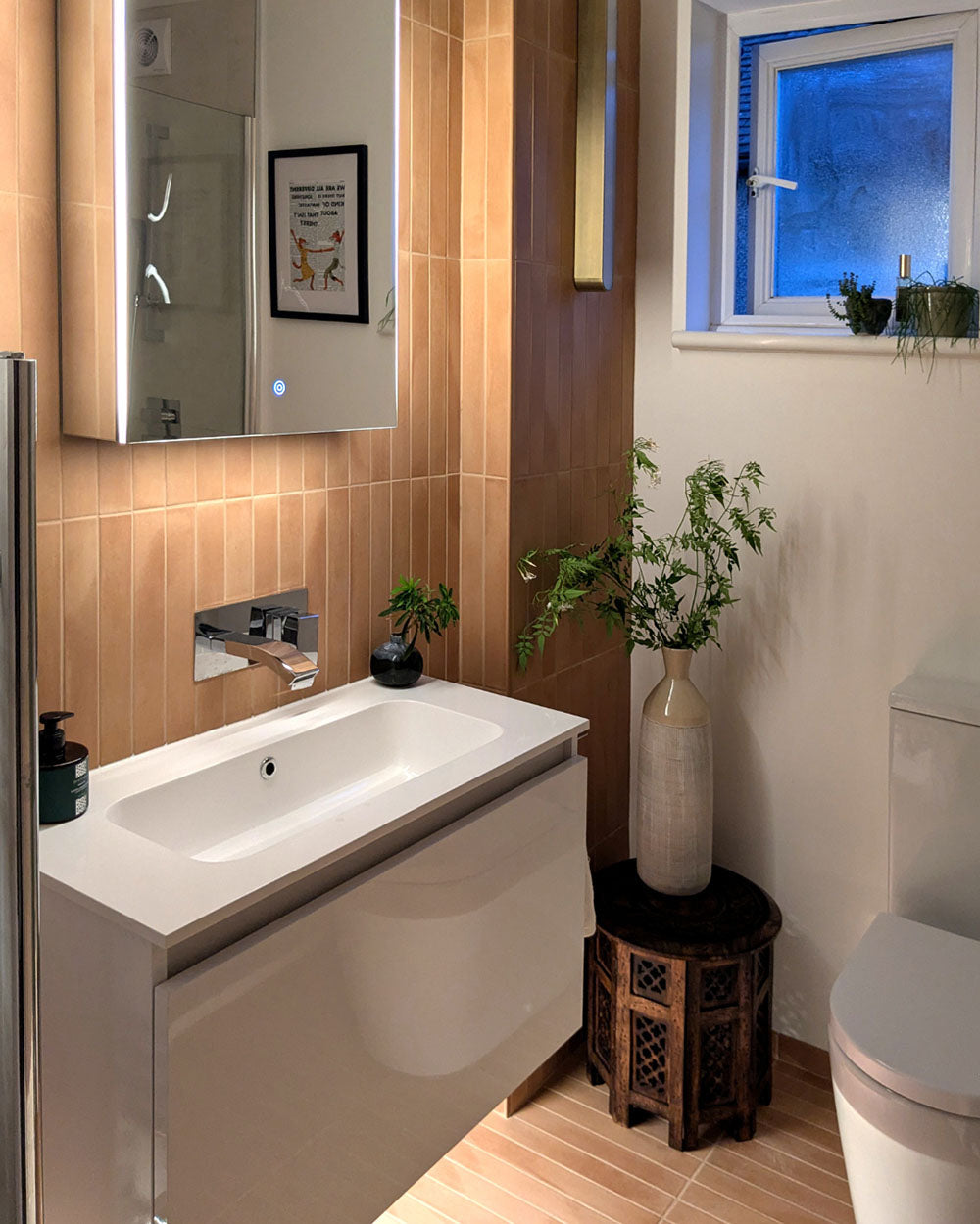 Contemporary bathroom featuring Jumairah Clay matt porcelain wall and floor tiles in a vertical stacked layout, paired with a floating white vanity, illuminated mirror cabinet, chrome brassware, soft neutral walls and natural wood accessories for a warm, minimalist interior.