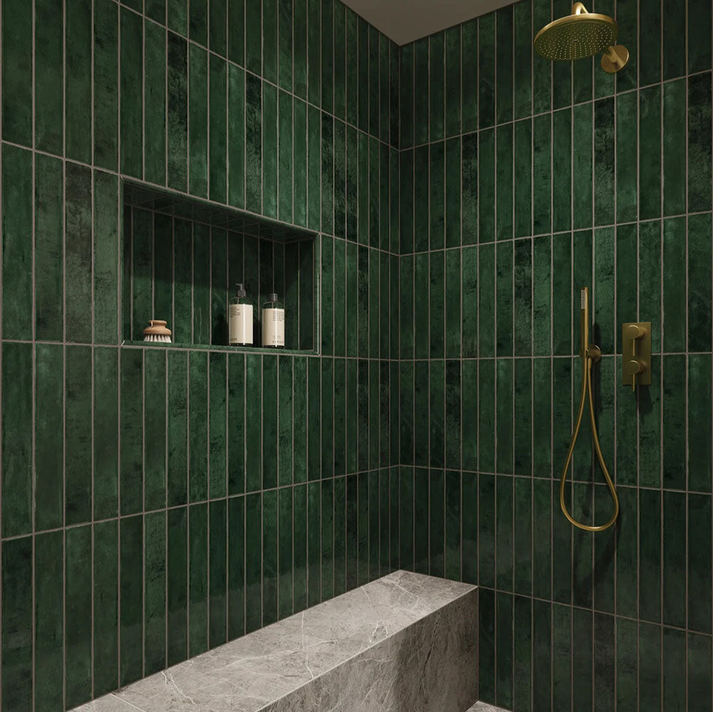 Walk-in shower featuring Jumairah Pine Forest Green 5 × 40cm gloss ceramic wall tiles, laid vertically with deep green tonal variation, paired with brass fittings, a built-in niche, and a marble-effect bench for a refined finish.