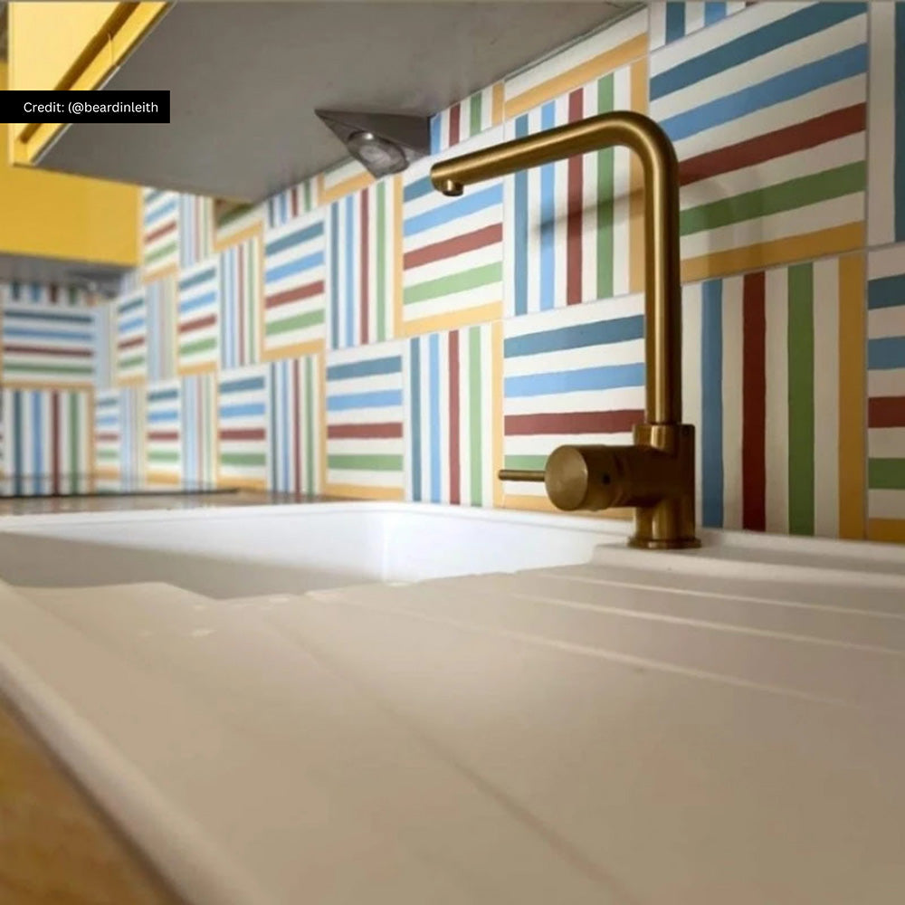Kitchen interior featuring Pinstripes Rainbow 20x20cm patterned tiles installed as a colourful splashback, styled with bold yellow cabinetry, wood worktops, and brass tap for a playful, contemporary design.