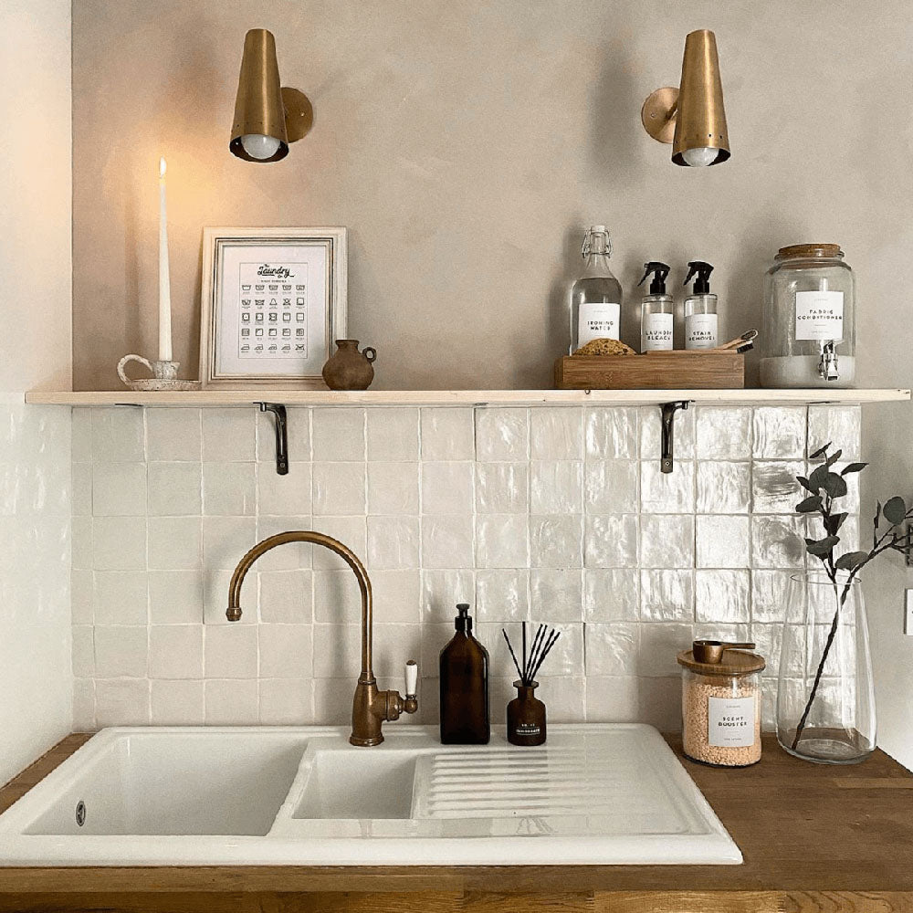 A warm, characterful kitchen splashback featuring Zellige Oyster Square Moroccan-style ceramic tiles in a 10 × 10cm format, with softly uneven edges and a gently reflective glazed finish that adds depth and artisanal charm. Paired with natural wood worktops and brass fittings, the tiles bring a calm, timeless feel with subtle variation and texture.