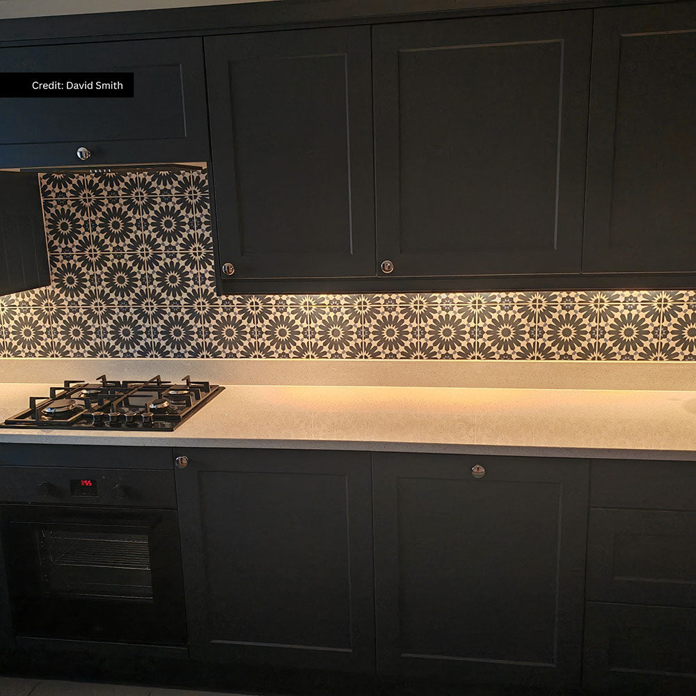 Kitchen setting featuring Fez Federal Blue 20x20cm Moroccan-style wall tiles, used as a patterned splashback, showcasing intricate geometric design, paired with dark cabinetry, light worktops and warm under-cabinet lighting.