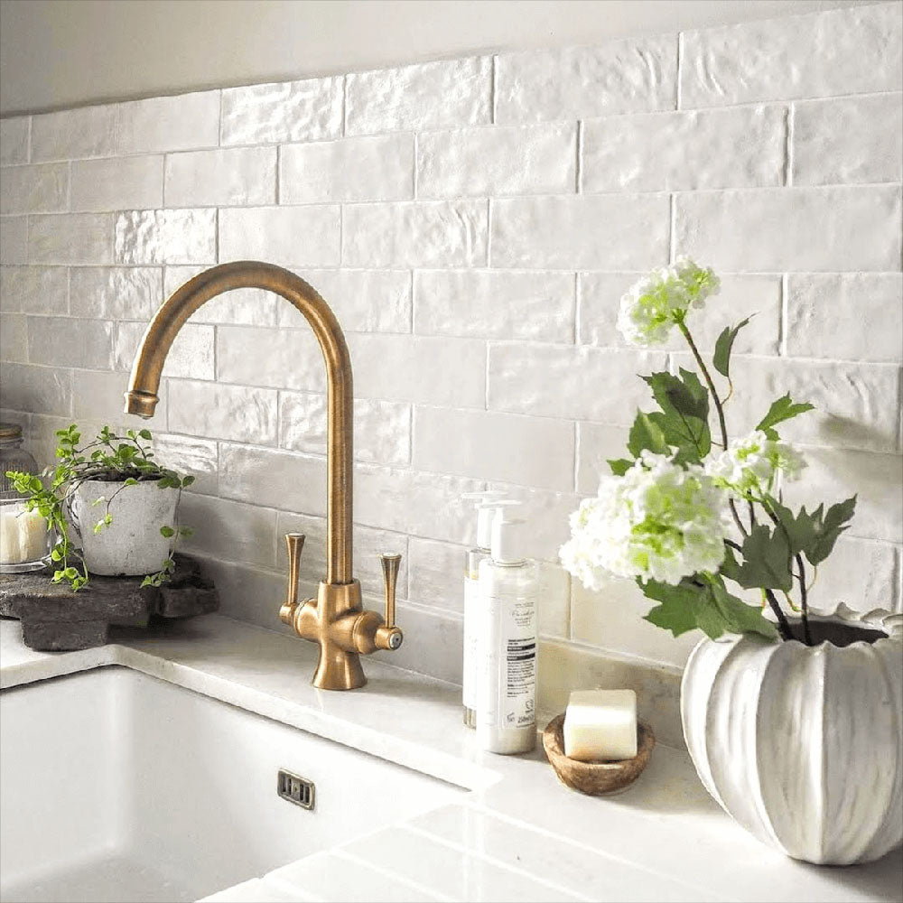Kitchen splashback featuring Zellige Oyster Brick Moroccan-style ceramic wall tiles in a 6.5 × 20cm brick format, laid in a staggered pattern to showcase the handmade-look surface and soft oyster tones, paired with a Belfast sink, brass tap and natural accessories for a timeless kitchen finish.