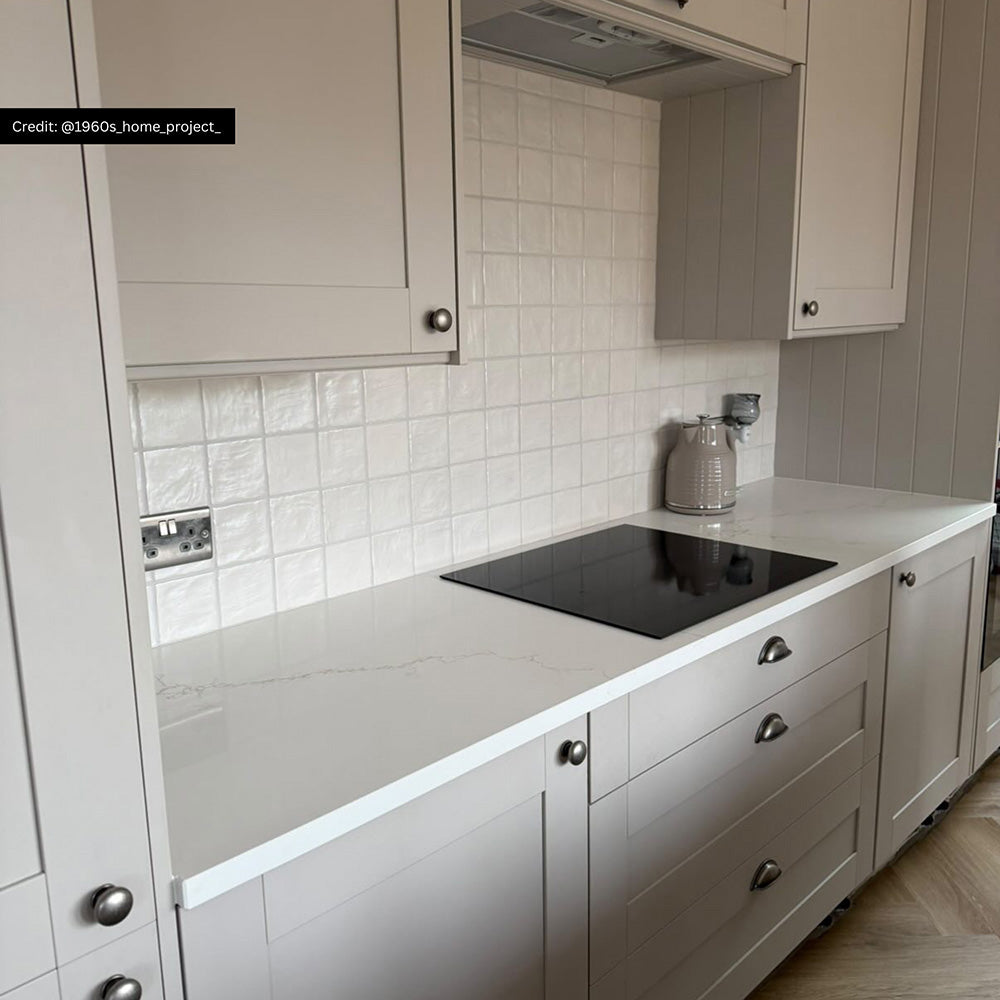 Kitchen splashback featuring Zellige Oyster Square Moroccan-style ceramic tiles in a 10 × 10cm format, laid in a neat grid pattern behind a hob and worktop, with softly uneven edges, a glossy oyster glaze and subtle tonal variation adding handcrafted texture to a classic neutral kitchen.