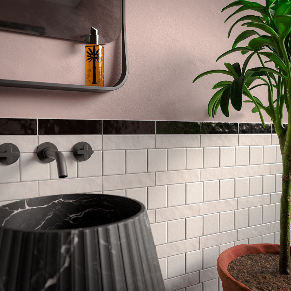 Bathroom featuring Levent Antique White Brick gloss porcelain wall tiles in 6cm x 24cm, showcasing soft antique white tones with a glossy finish, paired with a black marble border tile, blush pink walls, a fluted black marble pedestal basin, matt black brassware and a contemporary interior.
