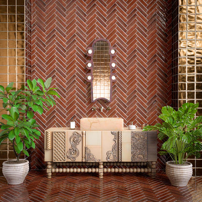 Statement bathroom featuring Levent Butterscotch Brick 6cm x 24cm gloss porcelain wall and floor tiles laid in a herringbone pattern, complemented by metallic mosaic accents, decorative vanity and lush indoor plants.