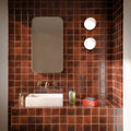Bathroom featuring Levent Butterscotch Square 10x10cm gloss porcelain wall and floor tiles, showcasing rich caramel brown tones with subtle shade variation, paired with a stone basin, brushed brass taps, an arched mirror and contemporary wall lights.