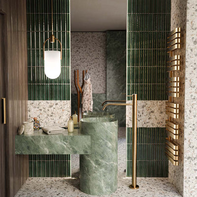 Bathroom featuring Levent Green Fluted Decor 6x24cm gloss porcelain wall tiles, showcasing deep green fluted detailing paired with terrazzo effect wall and floor tiles, green marble effect basins, brushed brass fittings and warm wood finishes for a luxurious contemporary space.