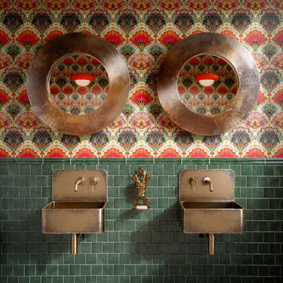 Bathroom featuring Levent Green Square 10x10cm gloss porcelain wall tiles, showcasing rich emerald green tones with subtle shade variation, paired with colourful patterned wallpaper, antique brass basins, round bronze mirrors and vintage-inspired brass fittings.